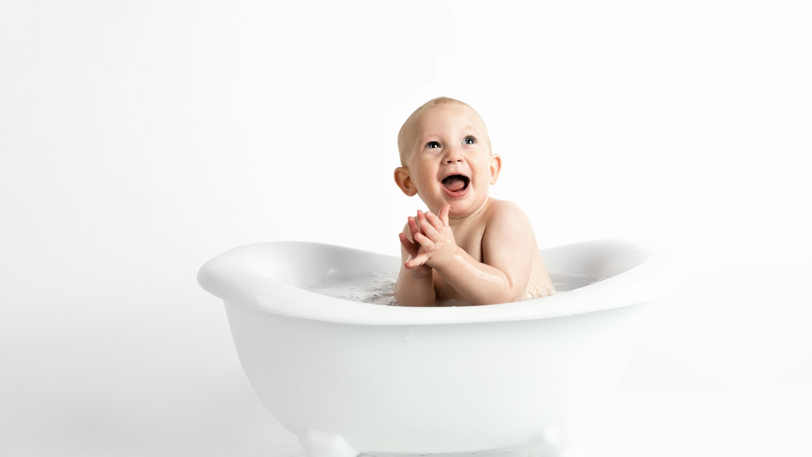 Happy baby sitting in a small white bathtub