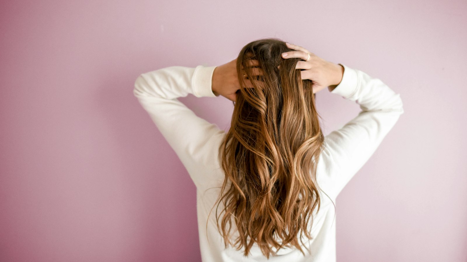 Woman with long wavy hair seen from behind against a pink wall