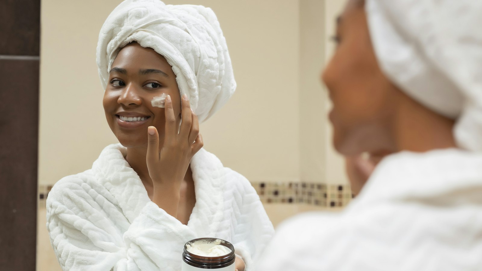 Smiling woman in a bathrobe applying moisturiser to her face